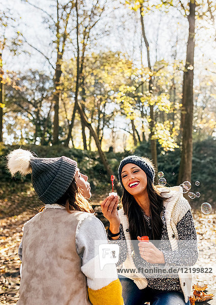 Zwei hübsche Frauen haben Spaß mit Seifenblasen im herbstlichen Wald