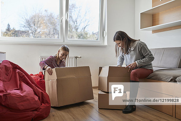 Two young women unpacking cardboard boxes in a room