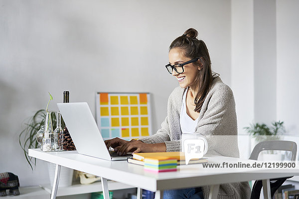 Smiling young woman at home using laptop on desk