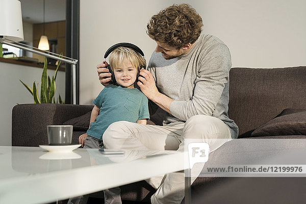 Father putting on headphones on son on couch at home