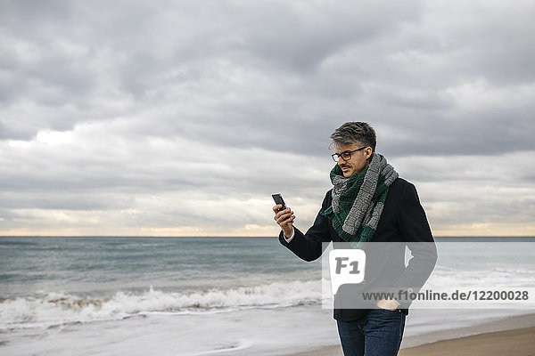 Geschäftsmann am Strand mit Blick aufs Handy