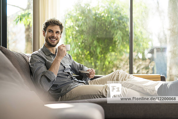 Laughing man relaxing on couch at home drinking coffee