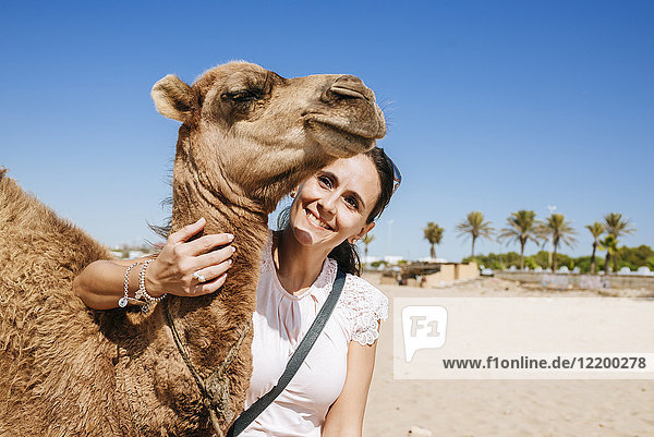 Marokko,  Tanger,  Porträt der lächelnden Frau mit Kamelbaby am Strand
