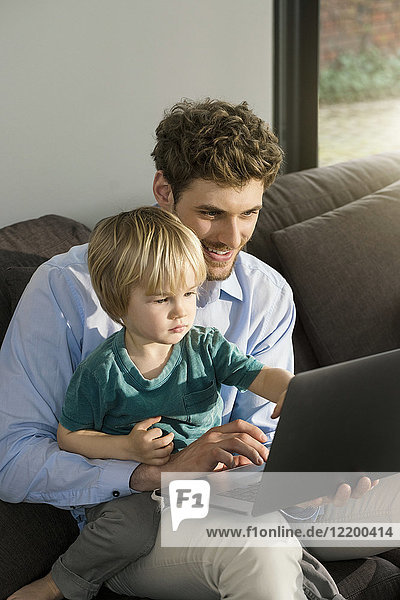 Father and son looking at laptop on couch at home