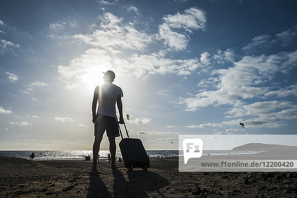 Man standing with rolling suitcase at the beach