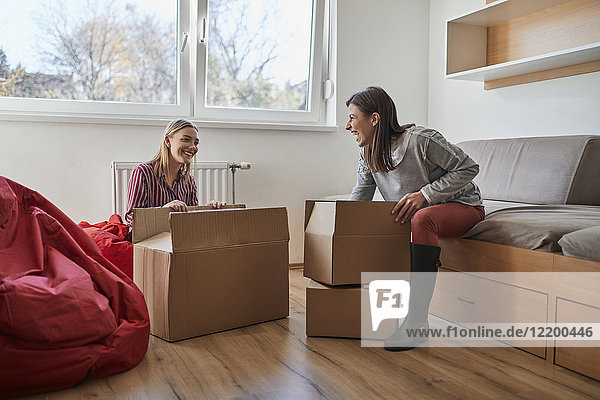 Two happy young women unpacking cardboard boxes in a room