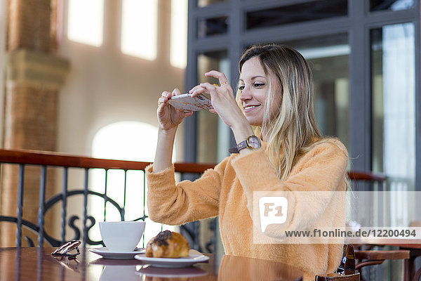 Lächelnde junge Frau in einem Café beim Fotografieren von Handys
