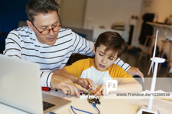 Vater und Sohn bauen einen Baukasten mit Laptop und Windturbinenmodell zusammen