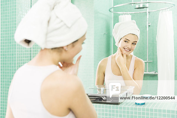 Junge Frau beim Auftragen der Feuchtigkeitscreme am Spiegel im Bad