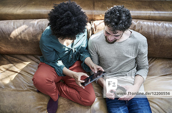 Young man and young woman sitting on couch with cup of coffee and tablet