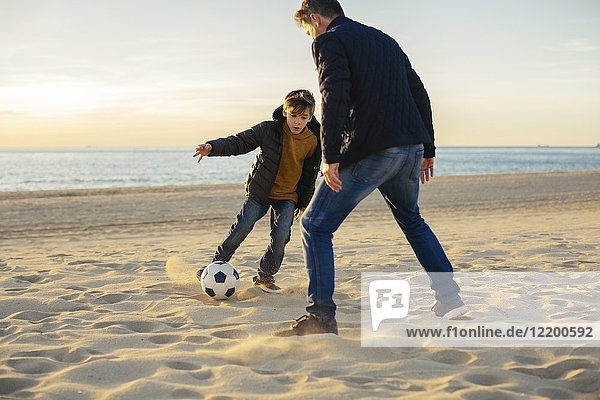 Father and son playing football on the beach