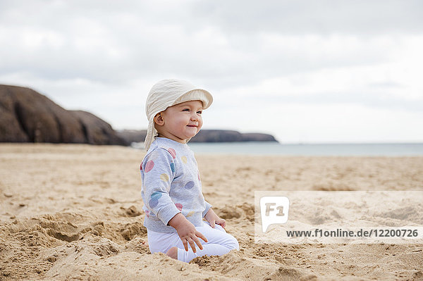 Spanien,  Lanzarote,  zufriedenes kleines Mädchen am Strand hockend