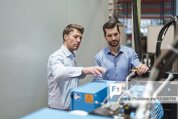 Two men discussing at machine in factory