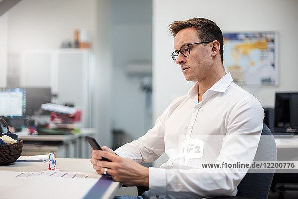 Young businessman using cell phone at desk in office