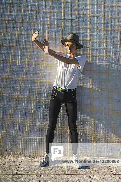 Woman wearing hat standing in front of tiled wall at sunlight