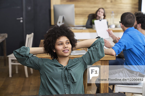 Young woman thinking in office with coworkers in background