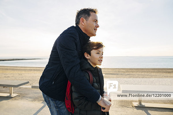 Vater und Sohn mit Roller auf der Strandpromenade bei Sonnenuntergang