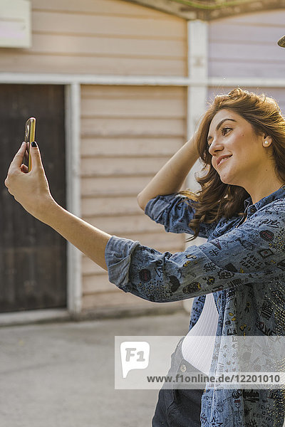 Lächelnde junge Frau nimmt Selfie mit Handy
