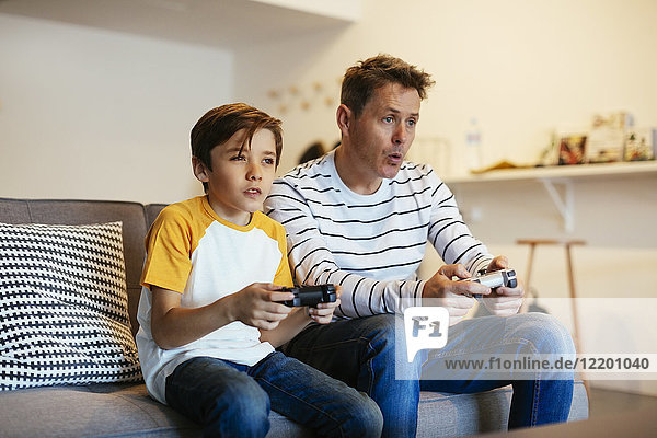 Father and son playing video game on couch at home
