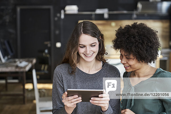 Two smiling young women sharing tablet in office
