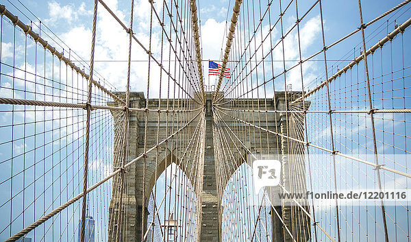 USA  New York  Brooklyn  Nahaufnahme von Brooklyn Bridge Metallkabeln und Bögen mit amerikanischer Flagge an der Spitze