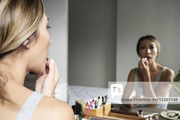 Woman at home using makeup applying lipstick in front of a mirror