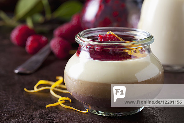 Glas Pudding mit Vanillesauce und Himbeersauce garniert mit Himbeeren und Orangenschale
