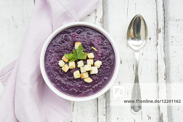 Bowl of red cabbage soup garnished with croutons and leaf of parsley