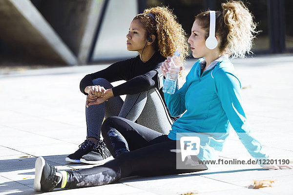 Two sportive young women having a break listening to music