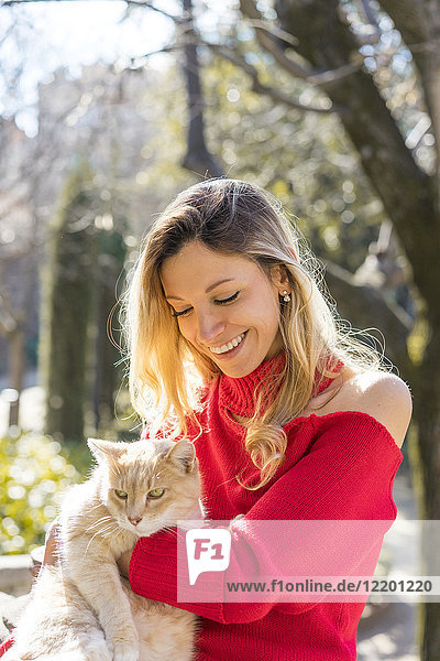 Happy young woman holding a cat in a garden