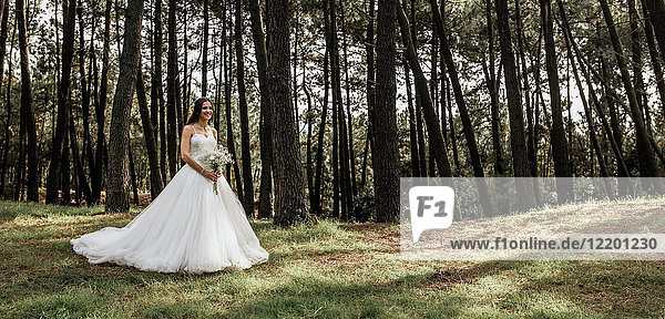 Lächelnde Braut mit Blumenstrauß im Wald