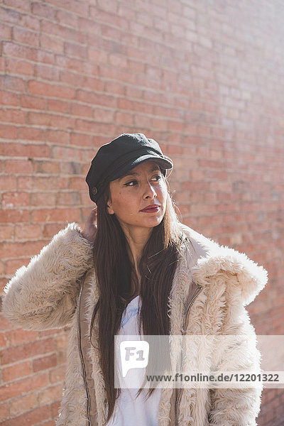Stylish young woman in front of brick wall