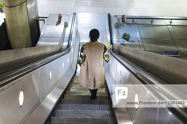Rückansicht der Geschäftsfrau auf der Rolltreppe der U-Bahn-Station