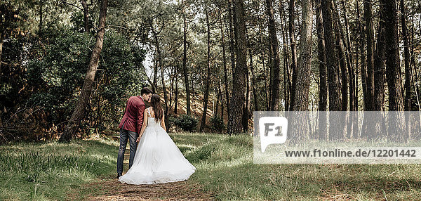 Rückansicht von Braut und Bräutigam beim Küssen im Wald