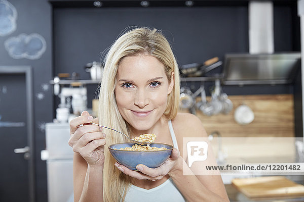 Porträt einer lächelnden blonden Frau in der Küche beim Müsliessen