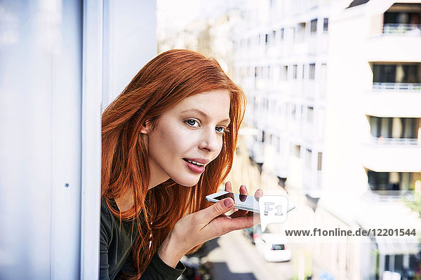 Porträt einer rothaarigen Frau am Telefon  die sich aus dem Fenster lehnt.