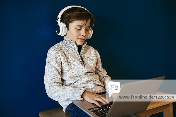 Junge sitzt auf der Bank  trägt Kopfhörer und benutzt einen Laptop.