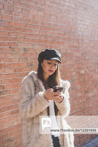 Stilvolle junge Frau vor der Ziegelwand mit dem Handy