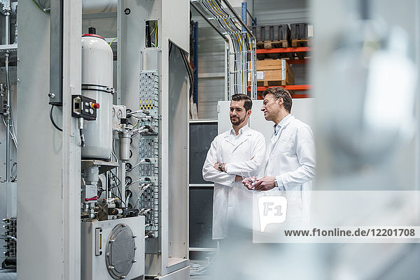 Two men wearing lab coats in factory looking at machine