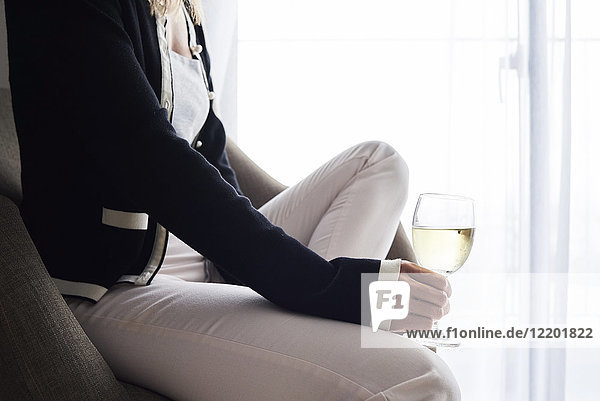 Nahaufnahme einer Frau bei einem Glas Wein zu Hause im Sessel sitzend