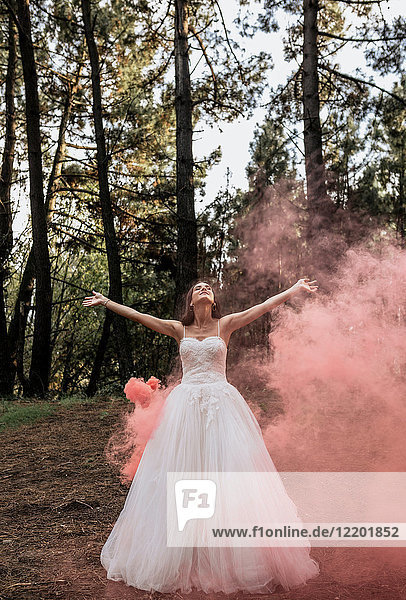 Woman wearing wedding dress in forest surrounded by clouds of smoke