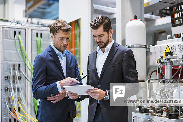Two businessmen in factory looking at tablet