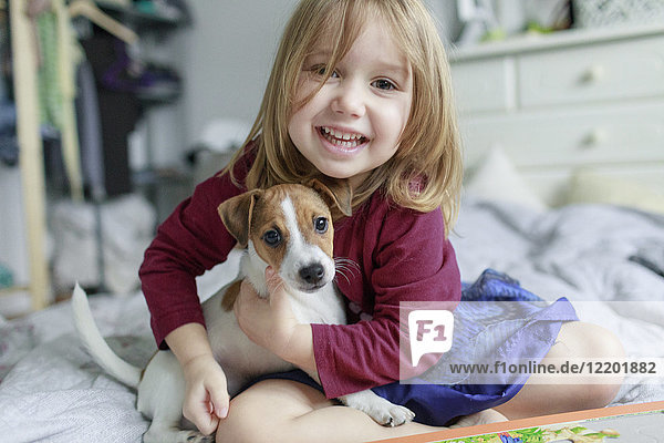 Portrait of happy little girl crouching on bed with Jack Russel Terrier puppy