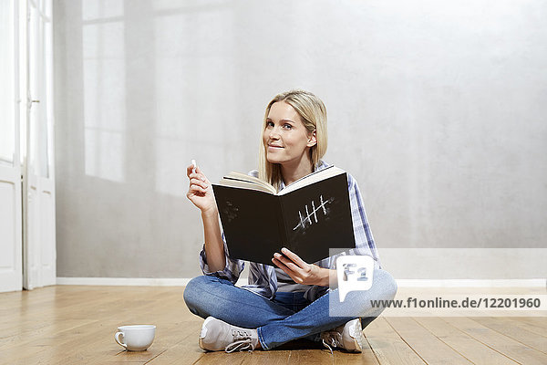 Porträt einer lächelnden blonden Frau mit Buch auf dem Boden sitzend