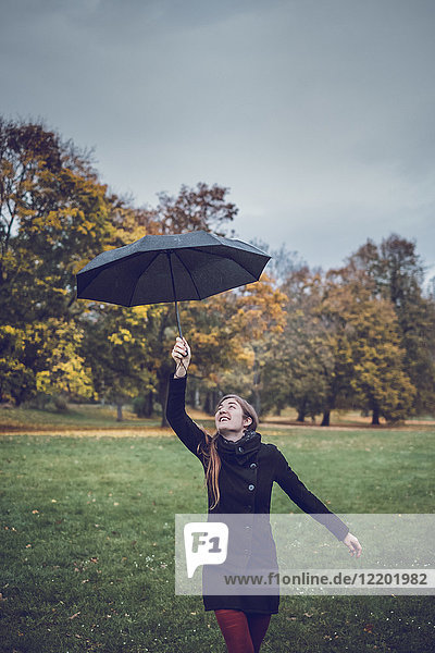 Fröhliche junge Frau tanzt mit Regenschirm im herbstlichen Park