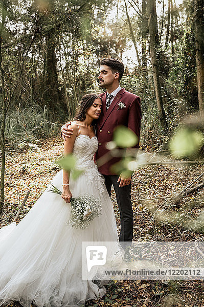 Groom embracing bride with closed eyes in forest