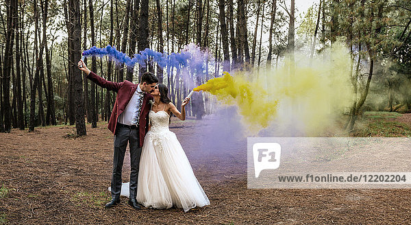 Braut und Bräutigam küssen im Wald mit Rauchfackeln