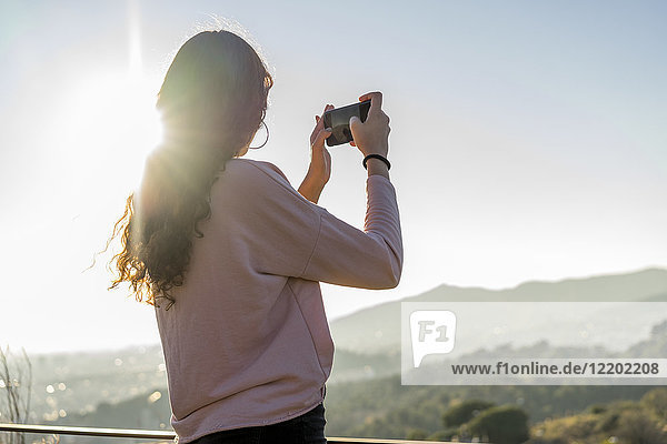 Young woman standing on a hill taking cell phone picture