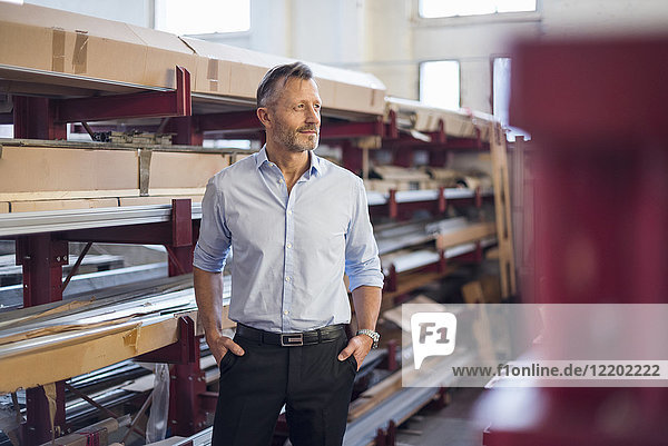 Mature businessman standing in factory storeroom looking sideways