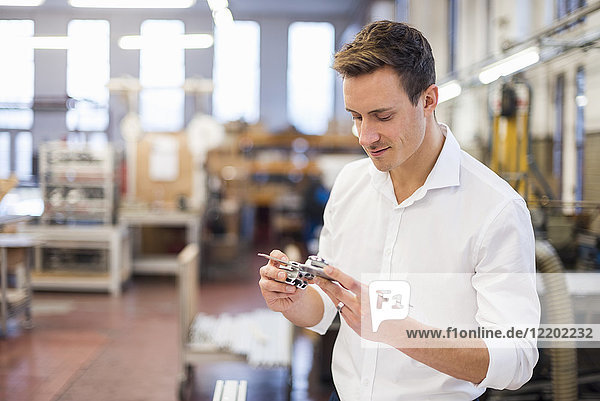 Young businessman in factory holding component